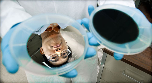 A silver wafer reflects the face of NREL research scientist Hao-Chih Yuan