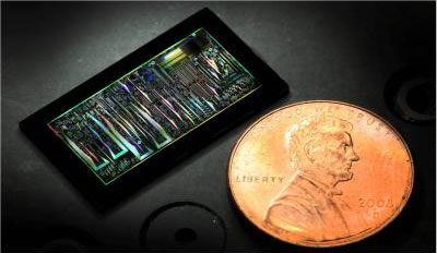 This is a dark-field optical image of a silicon photonic chip is shown in comparison to the size of a penny.