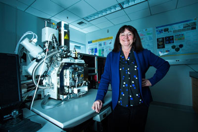 Tresa Pollock stands next to an electron microscope linked to a custom-made table mounted with a chamber used for advanced 3-D printing