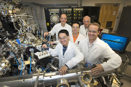 Collaborating scientists stand with the atomic layer-by-layer molecular beam epitaxy system