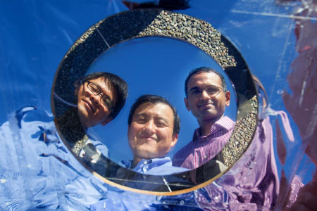 Stanford electrical engineering professor Shanhui Fan (center) gazes into the pizza- sized prototype with co-authors Linxiao Zhu (left) and Aaswath Raman
