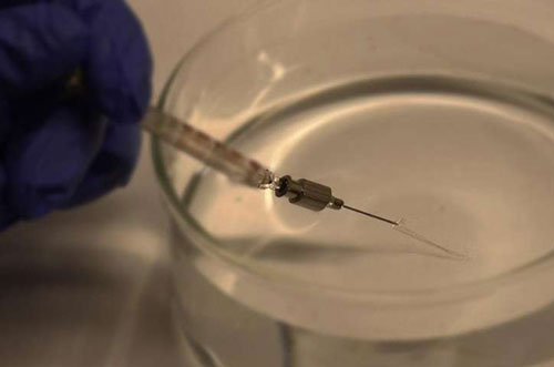 Photograph showing injection of mesh electronics through a metal needle into aqueous solution