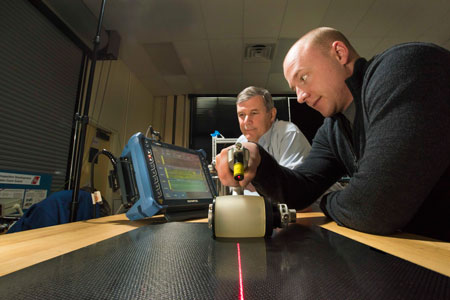 Sandia National Laboratories technologist Andrew Lentfer passes a roller probe over a composite as researcher David Moore checks data on a screen