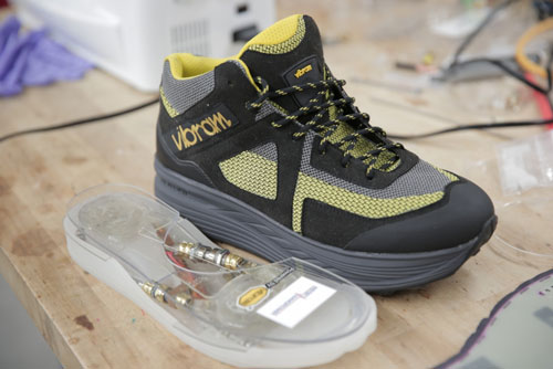 A shoe sole with an embedded energy harvester sits next to a first practical footwear energy harvester