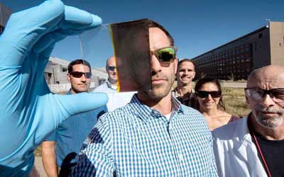 A scientist holds a piece of glass that is split between transparent and opaque