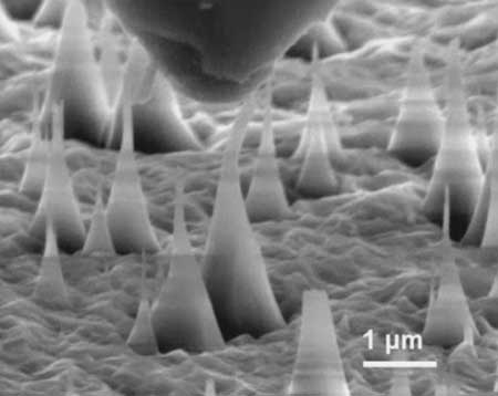 scanning electron microscope image of ultrafine diamond needles (cone shapes rising from bottom) being pushed on by a diamond tip