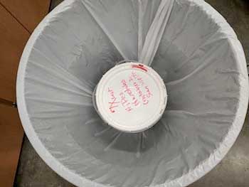 A plastic bucket and a plastic bag contain a 5-gallon supply of carbon nanotubes