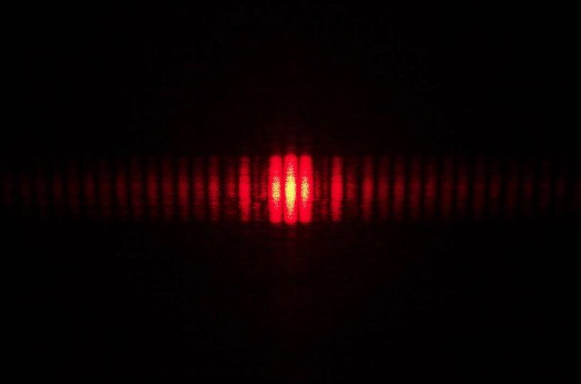In the double slit experiment, light passing through two slits produces two coherent sources of waves that interfere to form a bright spot in the center of the screen with a pattern of light and dark fringes on either side
