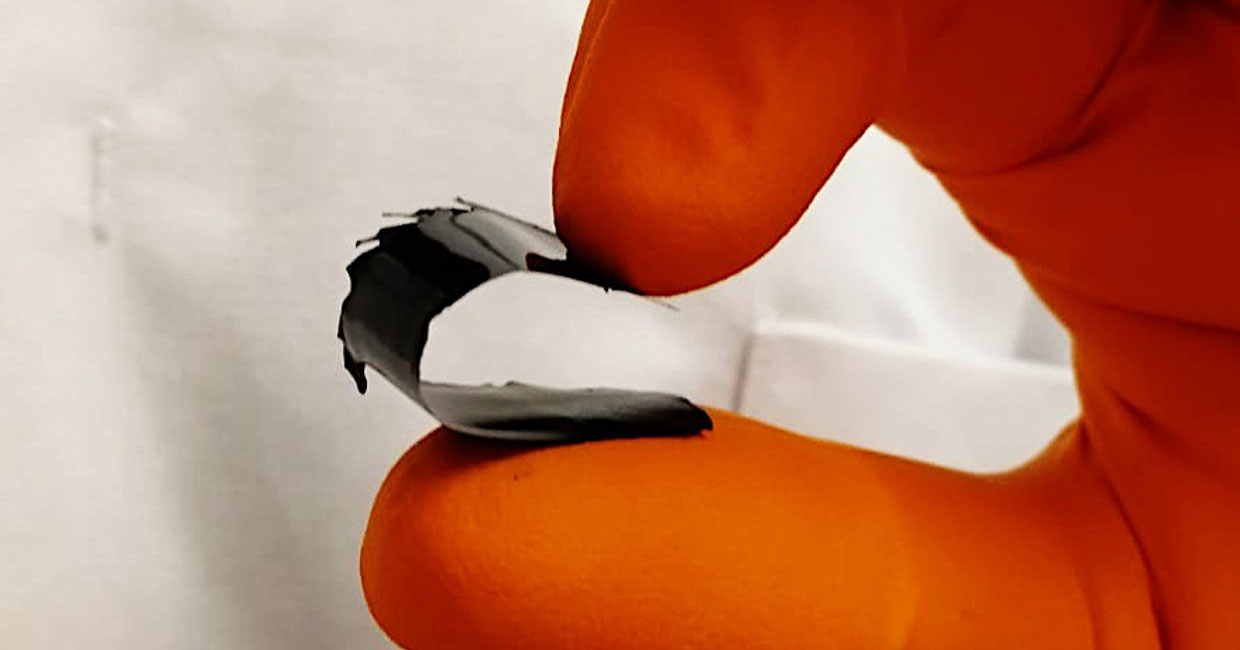 orange-gloved fingers bending a piece of black film