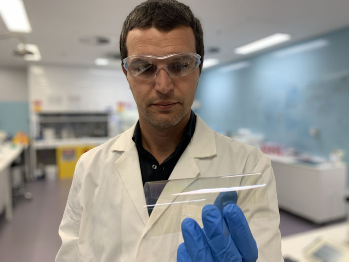 researcher in lab coat holding a transparent flexible electronis sheet