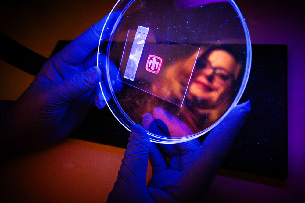 Materials scientist Dorina Sava Gallis shows a sample of an optical tag with the Sandia logo under an ultraviolet light