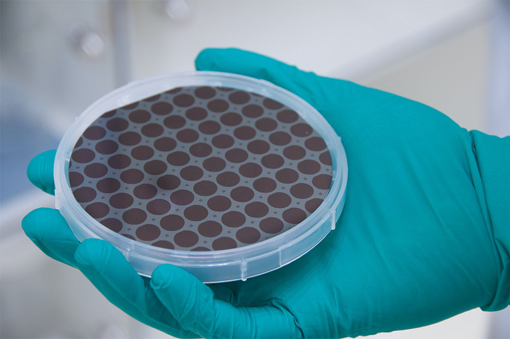 A patterned four-inch GaAs wafer with monocrystalline GaAs/AlGaAs dies that will eventually be fusion-bonded onto the coated silicon substrates