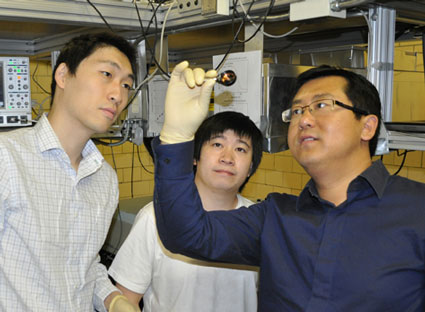 Iowa State physicist Jigang Wang, right, examines graphene monolayers grown on a substrate mounted in a cooper adapter as graduate students Tianq Li, far left, and Liang Luo