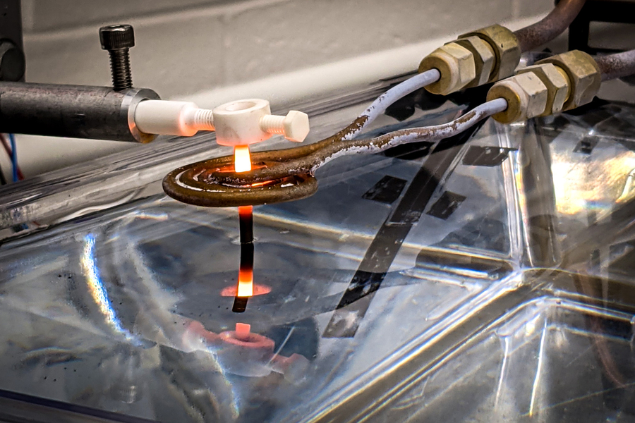 A thin rod of 3D-printed superalloy is drawn out of a water bath, and through an induction coil