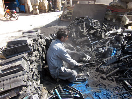 A man manually dismantling printers after which carcinogenic printer ink is left on the ground