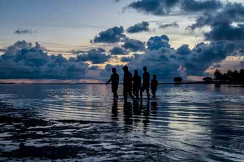 A group of people cross a shallow lagoon at dusk in the tropics