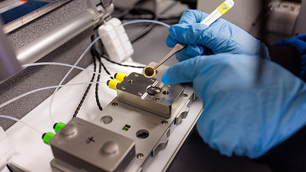 Researchers place a small, circular chip on an instrument to measure the adsorption of PFAS onto the molecular coatings