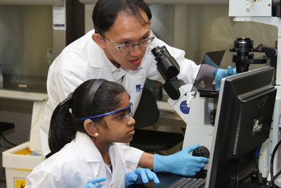 Losheni and Dr Meng Fatt Leong studying cells through a microscope