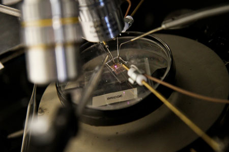testing a microplasma transistor by applying a voltage through four electrodes touching the surface of the transistor
