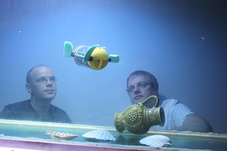 Researchers Asko Ristolainen and Taavi Salumäe looking the u-CAT swimming in an aquarium at Centre for Biorobotics