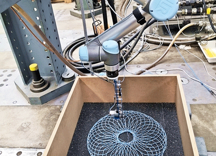 A robotic arm lays out a string in a mandala-like pattern on a bed of gravel