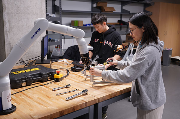 Two students in a lab working with robotic arm
