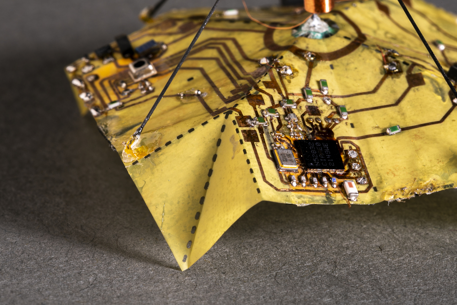 A close-up photo of a yellow device. The corner is folded and there are circuits patterned directly onto the material