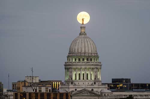 a supermoon rises in the nighttime sky behind the Wisconsin State Capitol
