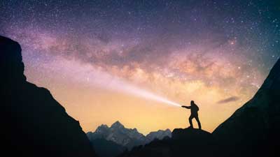man with flashlight on mountain against starry night background