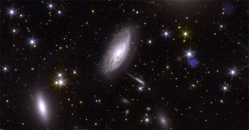 A tidy-looking picture with elliptical, bluish glowing spots of various sizes in the foreground, some with recognisable structures reminiscent of a vortex, against a black background with scattered sharp, bluish dots and yellowish diffuse spots